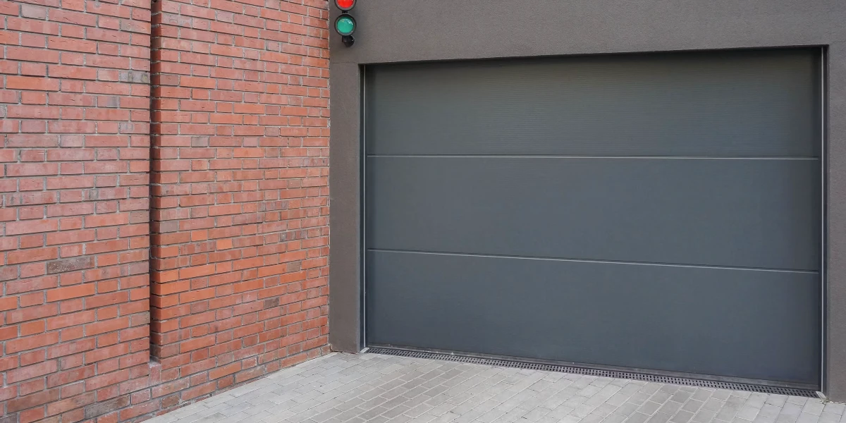a grey garage door next to a brick wall